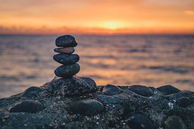 Stack of pebbles on beach against sky during sunset