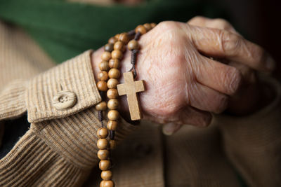 Midsection of senior woman holding wooden rosary beads with cross