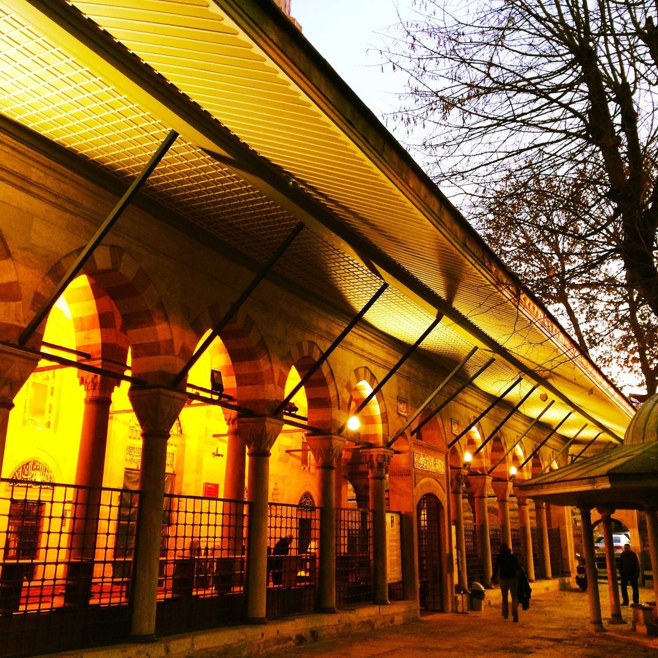 architecture, built structure, building exterior, illuminated, arch, city, low angle view, lighting equipment, incidental people, sky, architectural column, city life, travel destinations, yellow, building, facade, street light, travel, outdoors, ceiling