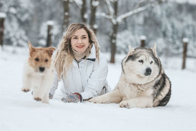 Smiling woman with dog sitting on snow covered land during winter