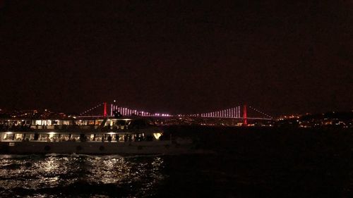 Illuminated bridge over river in city against sky at night