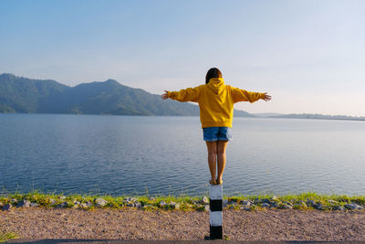 Rear view of young woman standing on bollard against lake