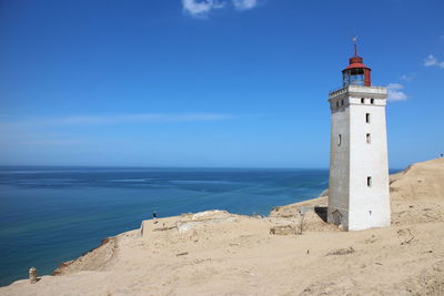 Lighthouse on beach against blue sky