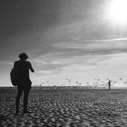 Rear view of silhouette man standing at beach against sky