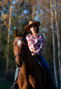 A woman wearing a cowboy hat rides a horse in a countryside farm yard,natural soft sunlight