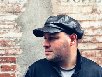 Close-up of mid adult man looking away while standing against brick wall