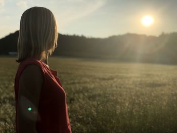 Side view of woman standing on land against sky during sunset