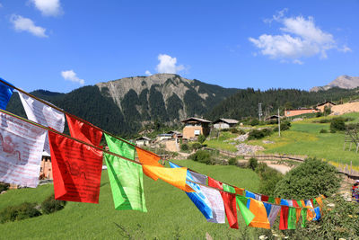 Multi colored flags hanging on field by mountains against sky