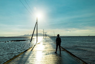 Rear view of man walking on beach against sky