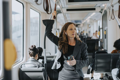 Female commuter holding smart phone while standing in train