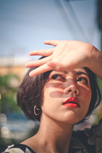 Woman looking away while shielding eyes in city