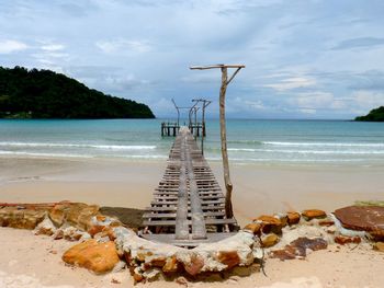 Pier over beach against cloudy sky