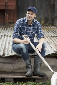 Full length of farmer with shovel sitting on corrugated iron at farm