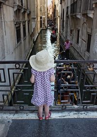 Rear view of girl looking at gondola in canal amidst buildings