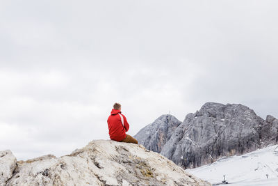 Person on rock by snowcapped mountain against sky