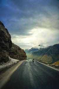 Young man riding motorcycle on road by mountains against sky