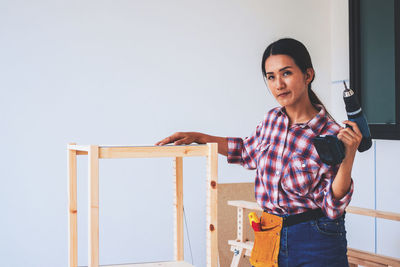 Portrait of smiling young woman standing against wall at home