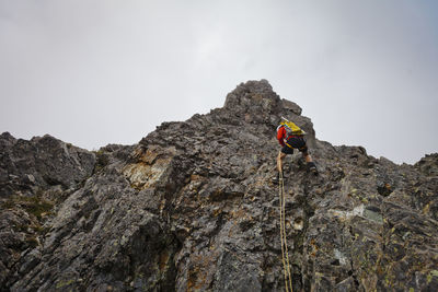 Low angle view of determined hiker climbing mountain against sky