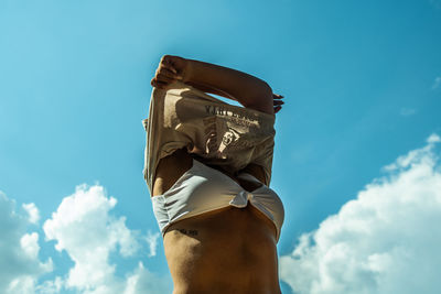 Low angle view of woman removing top against sky