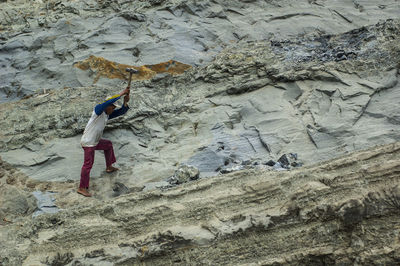 Side view of man hammering rock formations