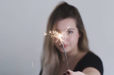 Woman holding illuminated sparkler against gray background