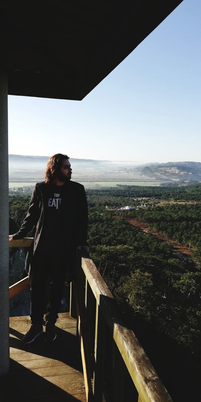 WOMAN STANDING ON RAILING AGAINST SKY