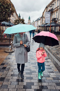 Mother and her little daughter holding the pink and blue umbrellas walking in a downtown