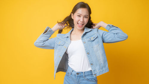 Portrait of smiling young woman against yellow background