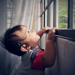 Portrait of cute boy looking through window at home