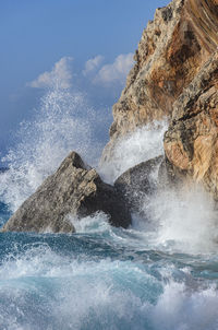 Sea waves splashing on rocks against sky