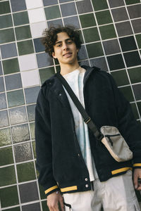 Low angle view of smiling teenage boy standing against tiled wall