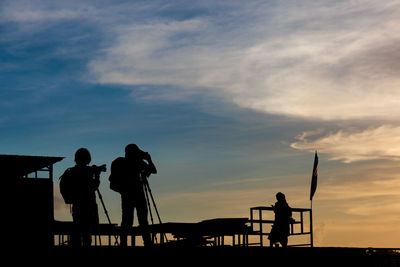 Silhouette people on shore against sky during sunset