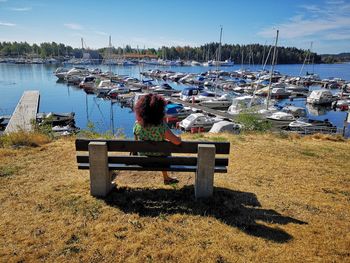 Rear view of woman sitting on bench at harbor