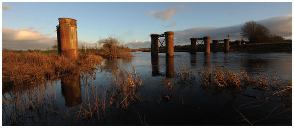 Wooden posts in lake against sky
