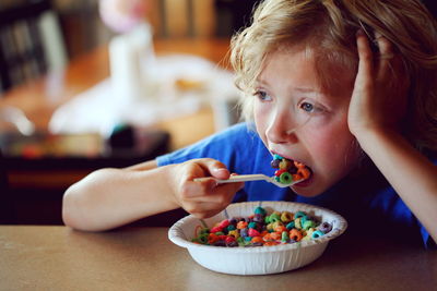 Close-up of thoughtful boy eating multi colored breakfast cereals on table