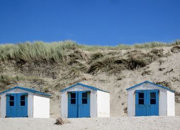 Huts at beach by sand dune against clear blue sky