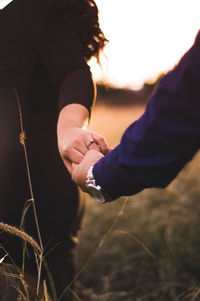 Midsection of couple holding hands on field during sunset