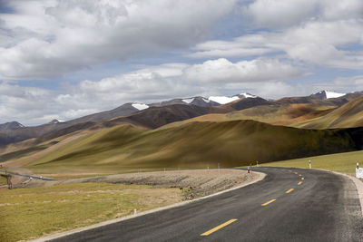 A flat, wide asphalt road leads to the beautiful and spectacular snow mountains in the distance