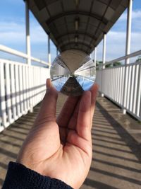 Cropped image of person hand holding bridge against sky