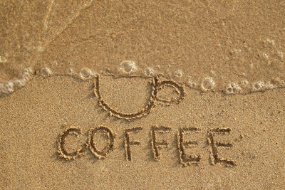 High angle view of coffee text on shore at beach