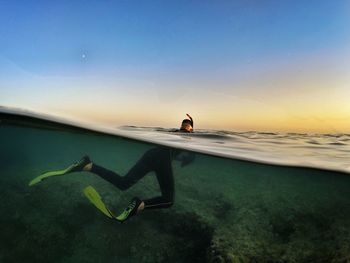 Man swimming in sea against clear sky during sunset