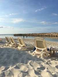 Deck chairs on beach against sky