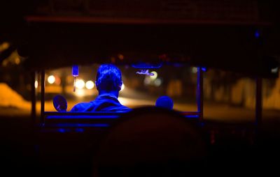 Rear view of driver in illuminated jinrikisha at night