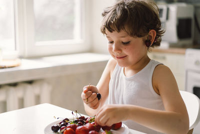 Cute beautiful little boy eating fresh cherry and strawberry.