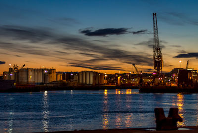 Illuminated cityscape by sea against sky at sunset