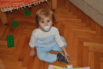 Portrait of cute boy sitting on wooden floor at home