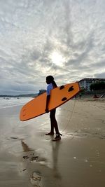 Full length of man with surfboard on beach against sky