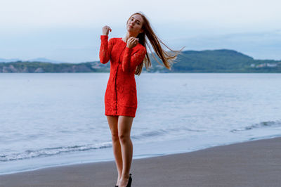 Portrait of young woman with tousled hair standing on shore at beach