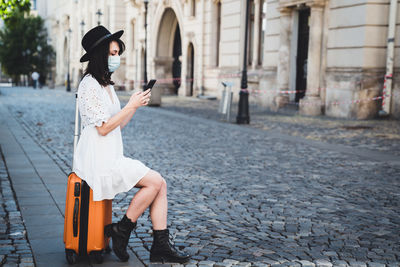 Full length of woman using smart phone sitting on street