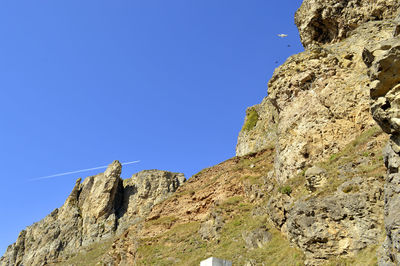 Low angle view of rocky mountain against clear blue sky